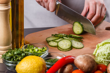 young woman in a gray apron cuts a cucumber