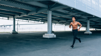 Fototapeta na wymiar Athlete running outdoors. Young sportsman with bare chest exercising near a bridge.