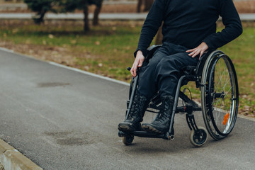 Close-up of male hand on wheel of wheelchair during walk in park