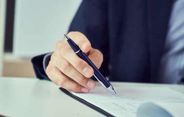 Businessman reading rental contract before making a deal. Corporate man with pen in hand working in modern office, signing business document on desk. close up.