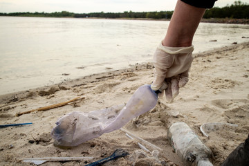 Young woman collects plastic garbage in a garbage bag on the sandy beach full of rigid plastic bottles and other garbage washed out on coast of the Kiev Sea. (Volunteering concept)