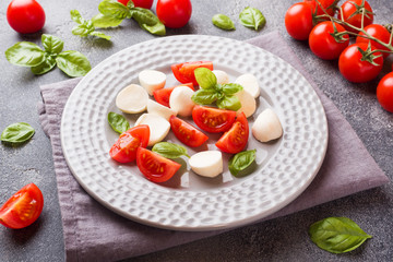 Caprese salad of tomatoes, mozzarella cheese and Basil on a dark background. Italian cuisine.