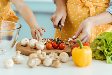 partial view of woman in polka dot apron vegetables on chopping board near daughter