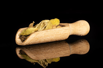 Lot of whole true cardamom pods in a wooden scoop isolated on black glass