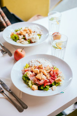 Plate of salad with tomatoes, jamon and baked vegetables on the white table. Glass of iced water with mint and lemon.