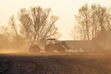 Fototapeta premium Sowing time. Blue tractor rides through the agricultural field in the sunlight.