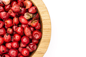 Closeup of lot of whole peruvian pink pepper in a wooden bowl flatlay isolated on white background