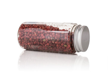 Lot of whole peruvian pink pepper lying on its side in a plastic bottle isolated on white background