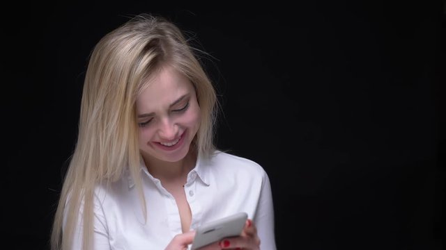 Pretty and young businesswoman in white shirt laughes watching into smartphone on black background.