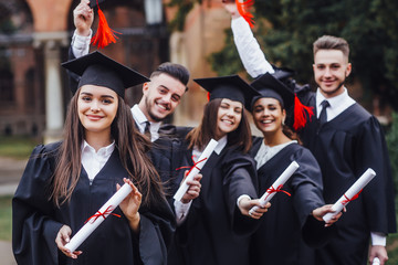She is in a black mortar board, with red tassel, in gown, with nice brown curly hair, diploma in...