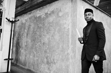 Obraz premium Strong powerful african american man in black suit and turtleneck and cap, with elephant tusk.