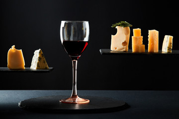 Fragrant red wine in glass beside sliced fresh cheese of different sorts