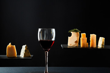 Fragrant red wine in glass beside sliced fresh cheese of different sorts