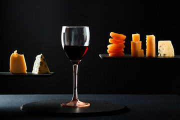Pieces of cheese and dried fruit beside glass of red sweet wine on black background