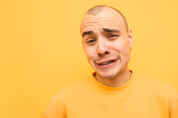 Obraz premium Сheerful guy in yellow clothes makes a funny face, a close-up portrait on a yellow background, wearing grillz teeth. Portrait of a fun rapper.