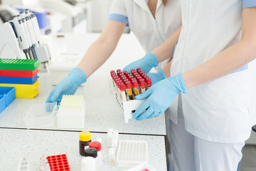 Hands of a lab technician holding a rack of color test tubes with blood samples of other patients.