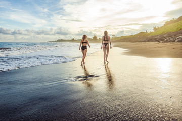 Two girl swimsuits walk on the beach.