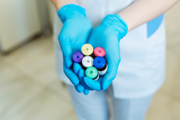 Hands of a lab technician holding a rack of color test tubes with blood samples of other patients.