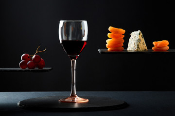 Pieces of blue cheese and dried fruit beside glass of red sweet wine on black background