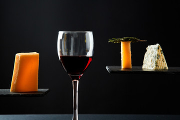 Red wine in crystal glass beside pieces of cheese on black background