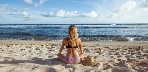 Girl sitting on the sand, back view and looking at the ocean. Banner panorama