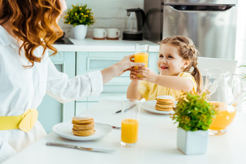 selective focus of mother giving glass with orange juice to smiling daughter while having breakfast