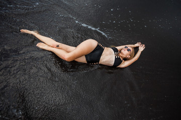 Fototapeta premium The girl in the swimsuit, lying on the black sand.