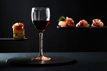 Composition of red wine in glass and pieces of meat snack on black background