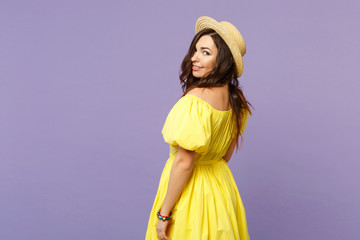 Side view of stunning smiling young woman in yellow dress, summer hat looking camera isolated on pastel violet wall background in studio. People sincere emotions lifestyle concept. Mock up copy space.