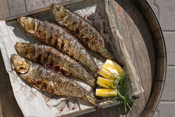 Grilled mackerel fish with baked vegetables on a wooden tray in the street, terrace, outdoor cafe,...