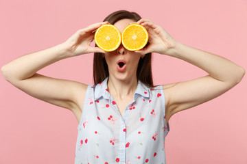 Amazed young woman keeping mouth open holding covering eyes with halfs of fresh ripe orange fruit isolated on pink pastel background. People vivid lifestyle relax vacation concept. Mock up copy space.