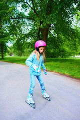 Cute little child girl learning to roller skate on beautiful summer day in a park. Child wearing...