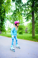 Cute little child girl learning to roller skate on beautiful summer day in a park. Child wearing...