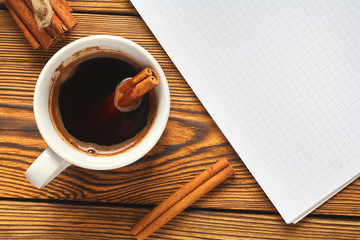 A bunch of cinnamon knitted with a rope, a cup of coffee and a notebook for writing on a wooden background close-up.
