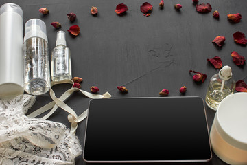 Composition with skin care cosmetic products without label and white lingerie on a black desktop background.