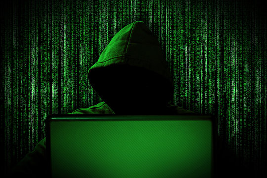 hacker with glowing mask behind notebook laptop in front of green source binary code background internet cyber hack attack concept