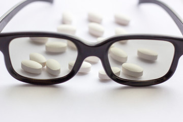 Fototapeta na wymiar Pills, capsules and tablets with glasses on light background. Pharmacy and medicine concept. Focused on a pharmaceutical industry for eye diseases. Selective focus photography