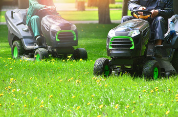 Two lawn mowers trimming green grass on a meadow.