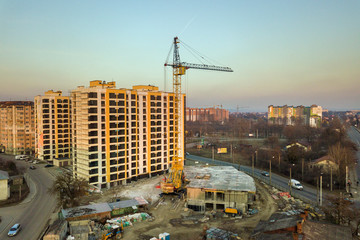 Aerial view of tall apartment building complex, unfinished building with scaffolding and tower crane on blue sky copy space background. Drone photography.