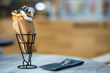 White plate with ice cream dessert in wafer cup with chocolate cookies and creative decoration topping on blurred colorful interior background.