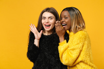 Two young women friends european and african american in black yellow clothes standing posing...