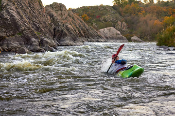 Man in green kayak fights with rapids of fast mountain river among the rocks. Whitewater kayaking, extreme water sport.