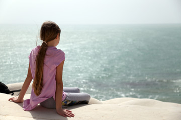 Fototapeta na wymiar Ragazzina seduta osserva ammirata il mare