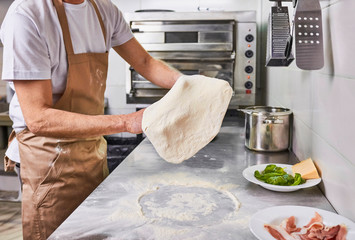 Chef tossing pizza dough at pizzeria kitchen