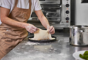 Processing of the pizza dough by the pizza maker at Italian restaurant kitchen 