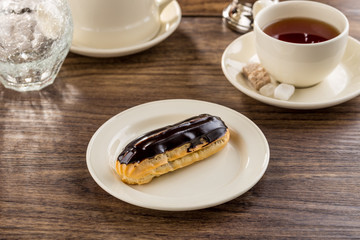 Homemade eclair dessert with chocolate sauce and cup of tea on wooden table