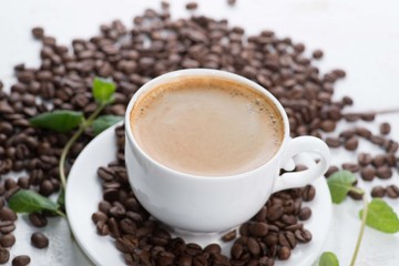 white cup of coffee on a background of scattered coffee beans on a white background
