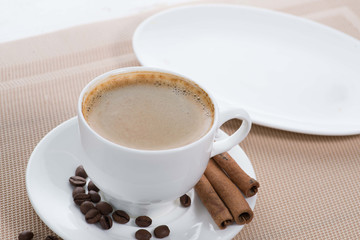 white cup of coffee on the background of scattered coffee beans and flowers