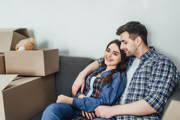 Happy couple relaxing on sofa having fun on moving day, excited young homeowners enjoying relocation in into new home.