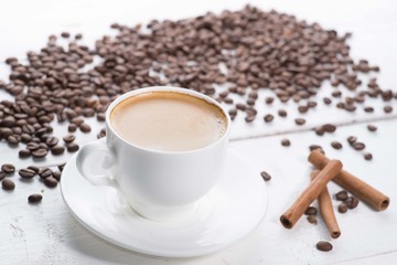 white cup of coffee on a background of scattered coffee beans on a white background